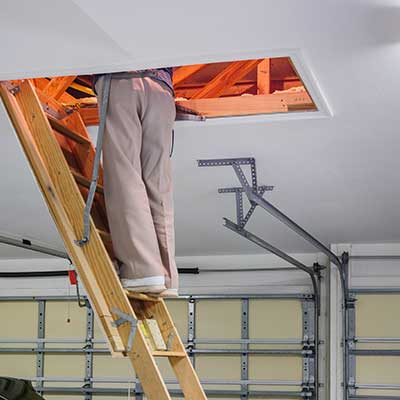 Worker on a wooden ladder that leads up to the attic, their top half physically inside of the attic space in order to inspect it