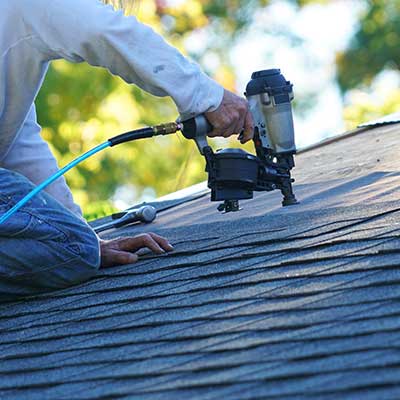 Close up of a worker installing shingles on a residential roof with a nail gun
